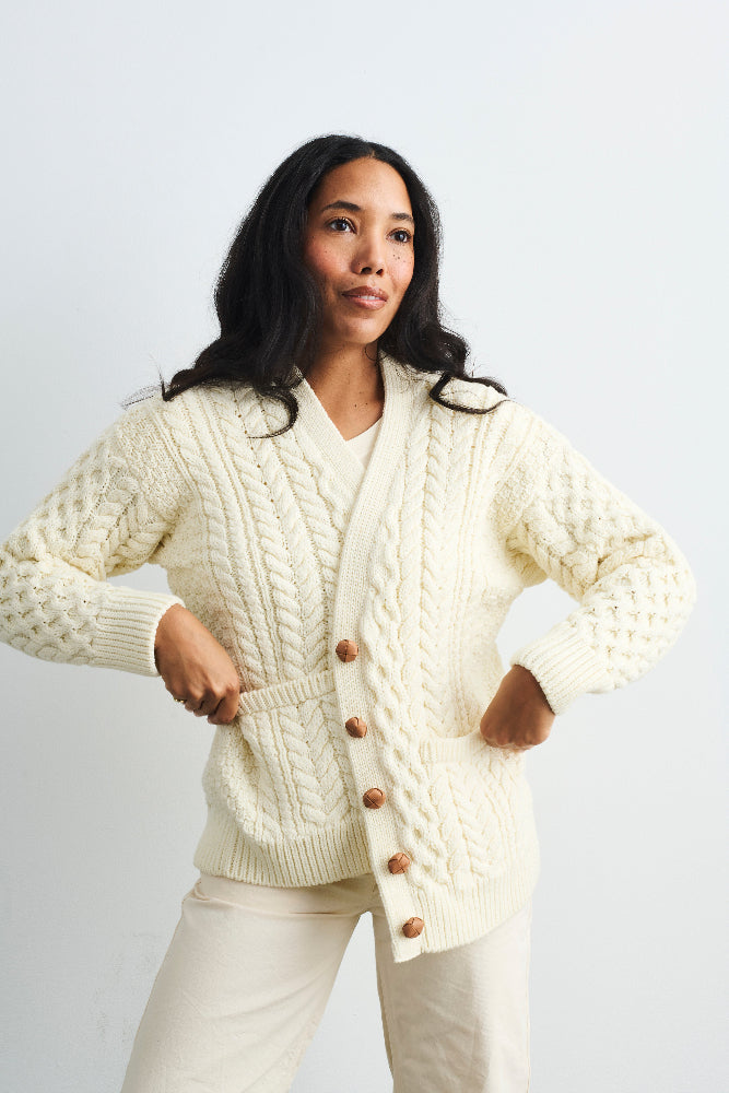 Woman wearing a cream-colored cable knit cardigan with buttons on a light gray background