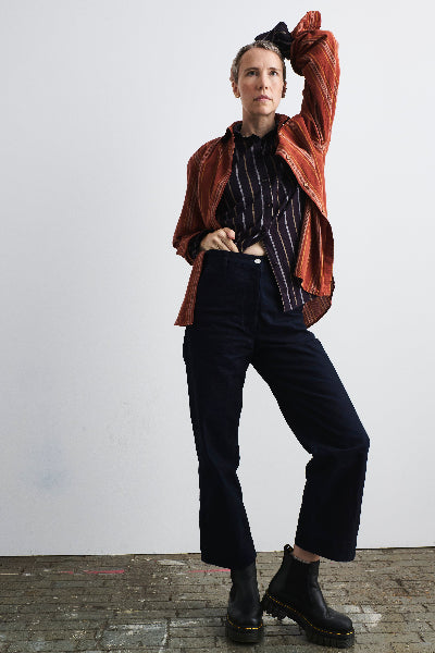 brushed cotton striped shirts rust layered over aubergine over indigo utility pants on tall short haired blond model standing on brick floor against white wall.
