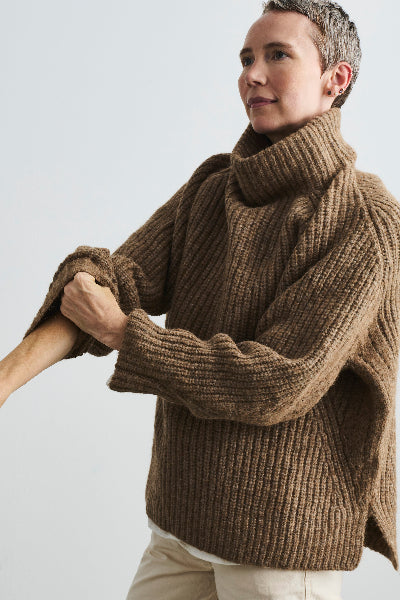 Person wearing a brown knitted sweater against a plain background
