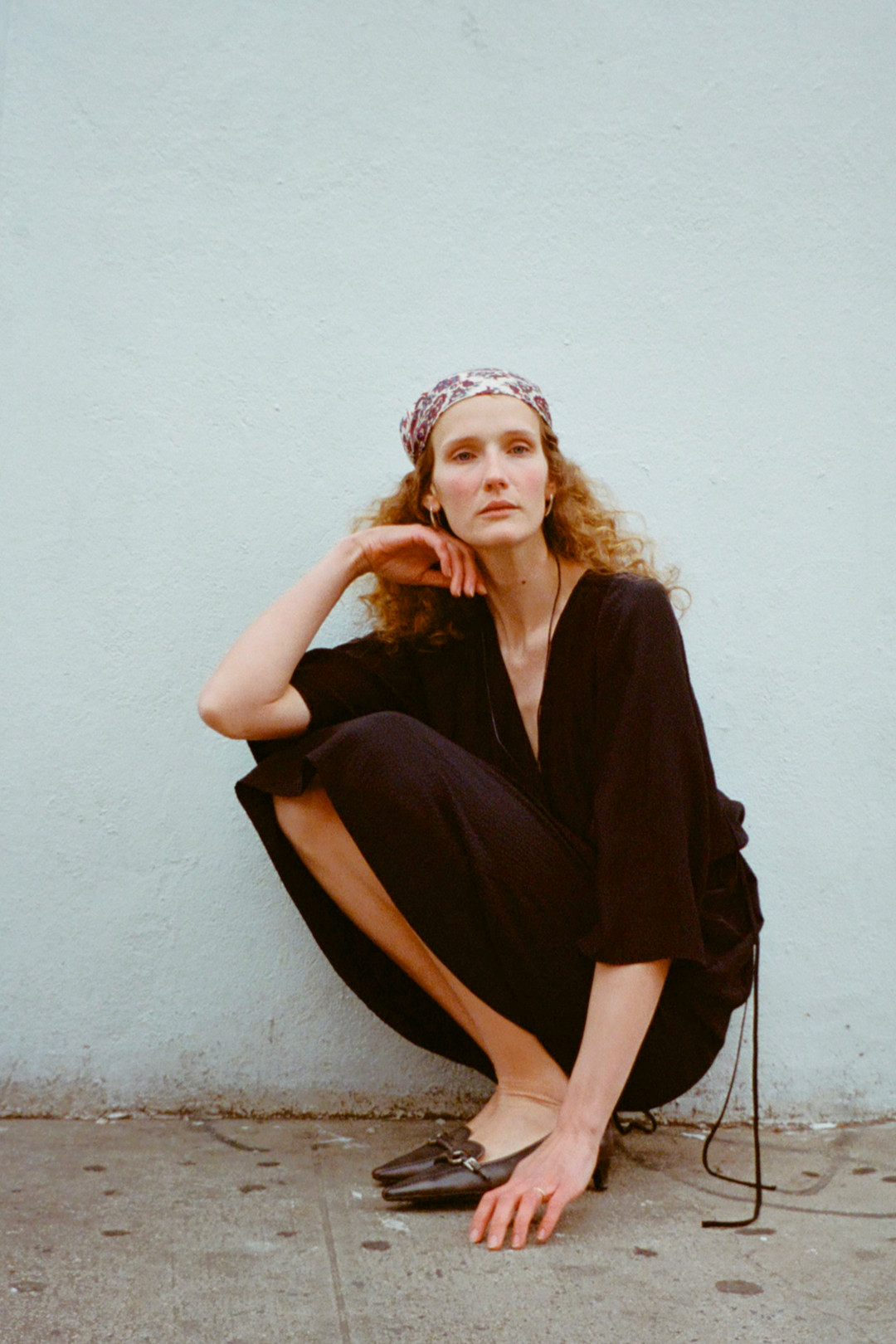 Woman in a four objects black sustainable silk dress sitting against a light blue wall.