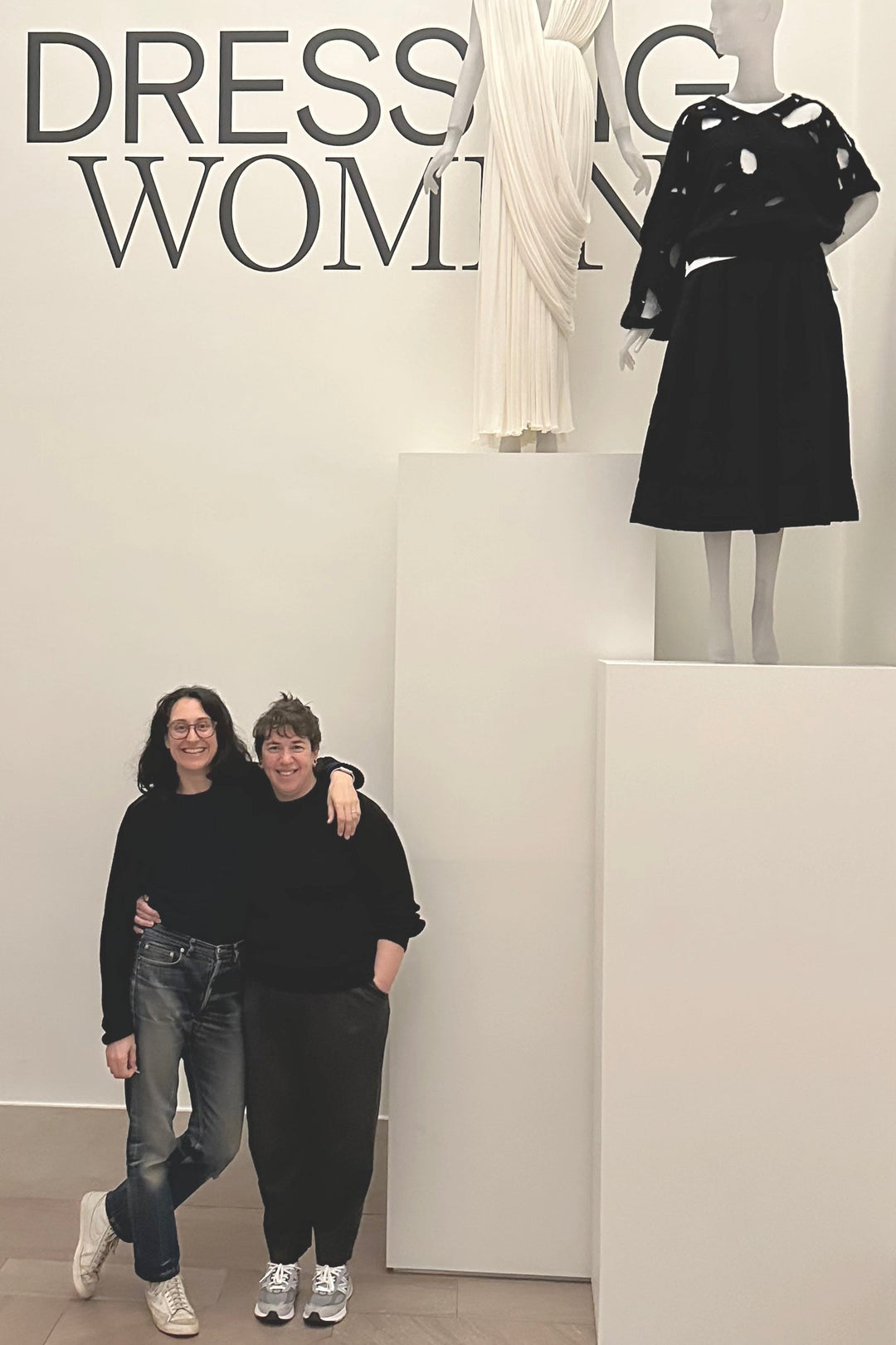 two people standing in front of a wall that says dressing women with a white and black dress on plinths