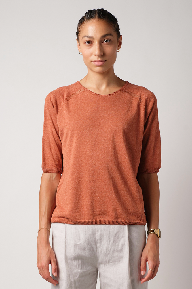 Person wearing a rust-colored short sleeve silk and linen sweater and LINEN PLEATED pants on a plain background