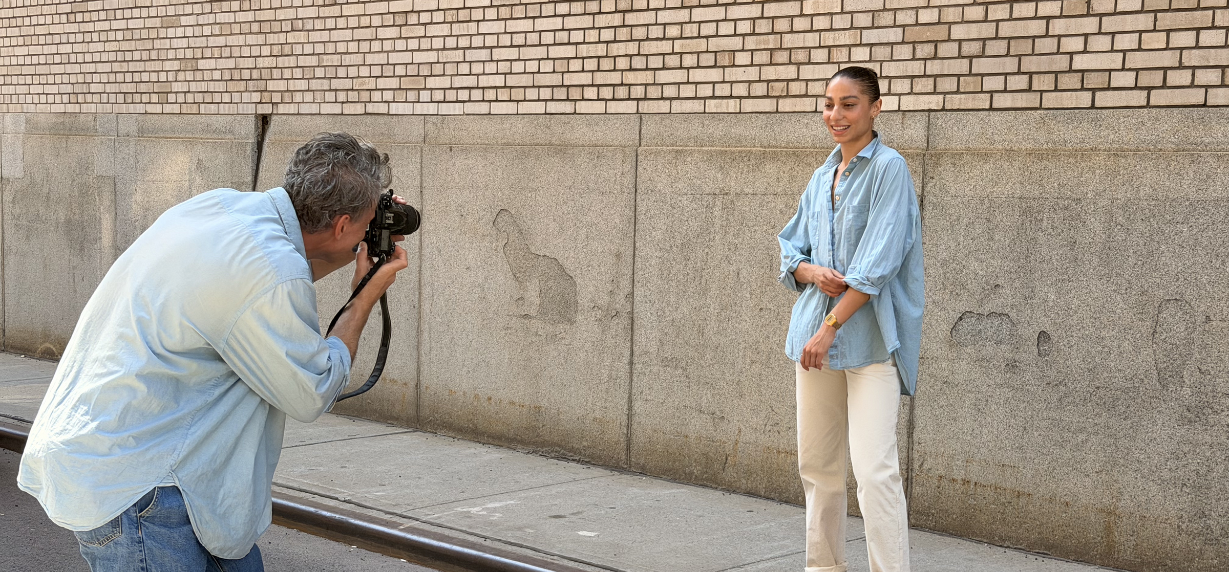 organic cotton denim chambray buttondown on model wearing white pants outside agains brick wall being phootgraphed by someone wearing the same shirt and jeans four objects