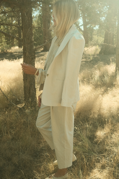 Person standing in a forest with tall grass, wearing a light-colored suit.
