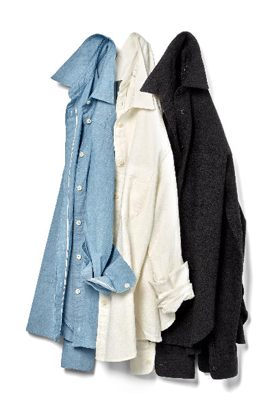 blue chambray, white linen and black wool buttondown shirts hanging in a row