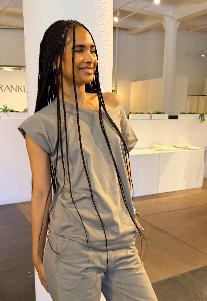 Person wearing a sage green outfit in an indoor setting with white walls and a counter.