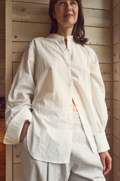 Woman wearing a white shirt organic cotton swiss dot buttondown and light-colored pants in a wooden interior setting
