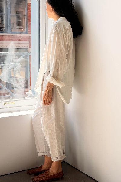 person standing in front of  window wearing a ling white shirt with cuffs rolled over linen pants with cuff rolled