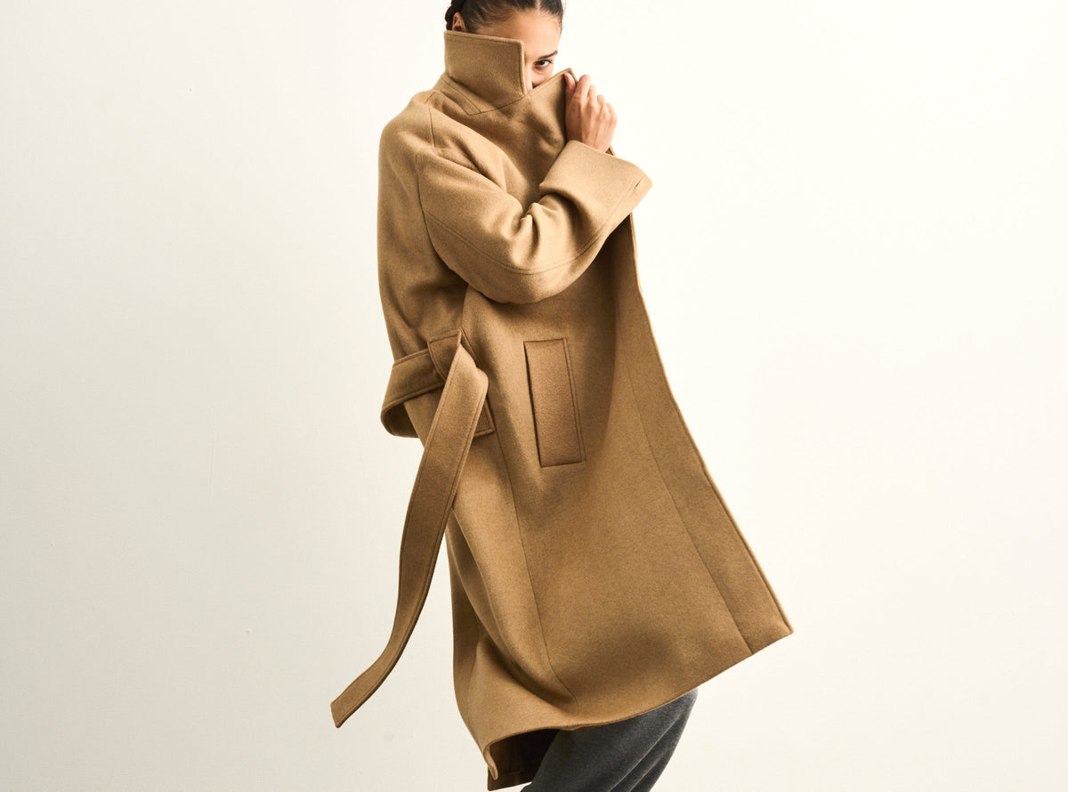 four objects camel overcoat on a woman with dark braids and grey merino sweatpants