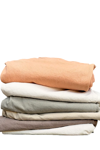 Stack of folded organic cotton pants in various colors on a white background.